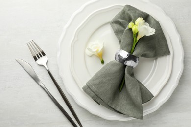 Stylish setting with cutlery, napkin, flowers and plates on light textured table, flat lay