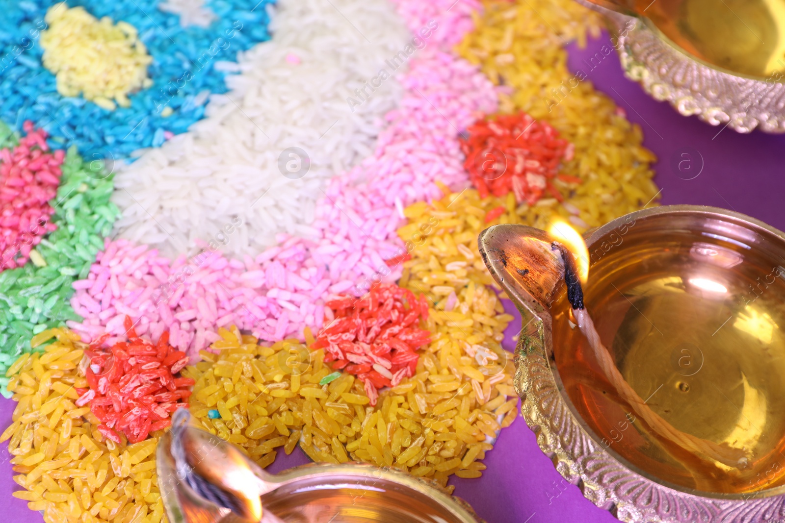 Photo of Diwali celebration. Diya lamps and colorful rangoli on purple background, closeup