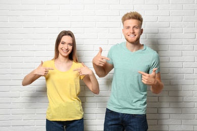 Photo of Young couple wearing blank t-shirts near white brick wall. Mockup for design