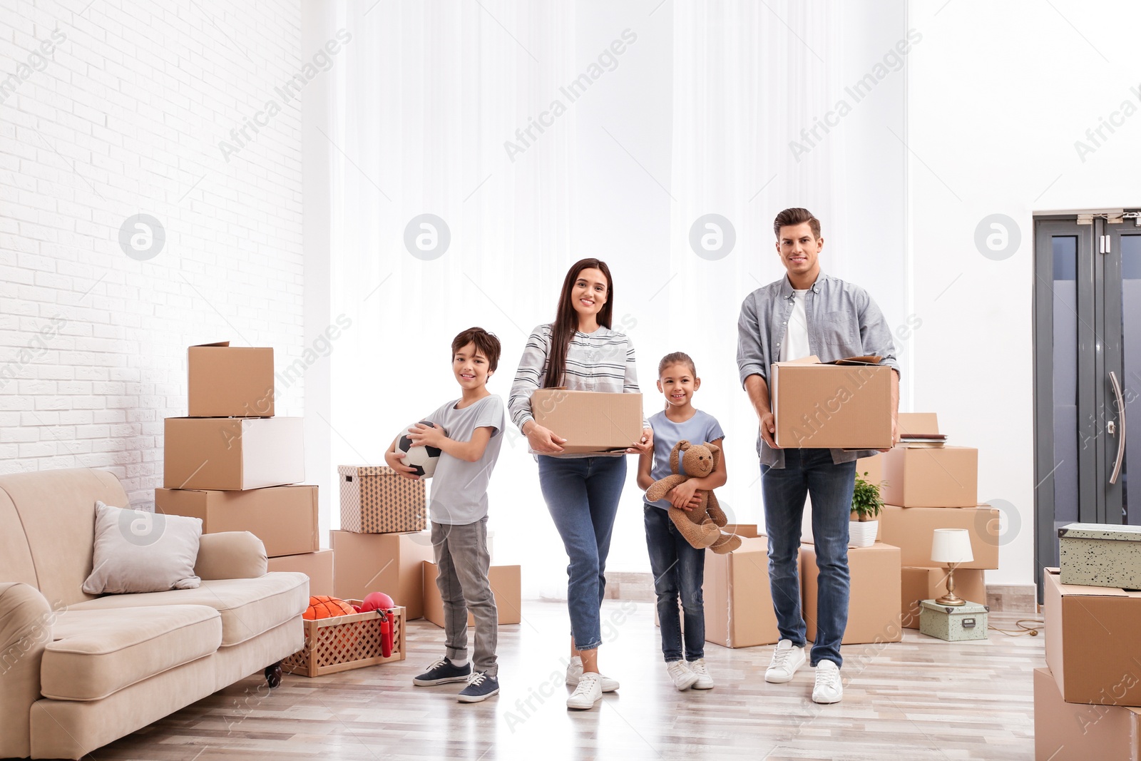 Photo of Happy family in room with cardboard boxes on moving day