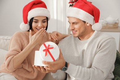Happy young couple with Christmas gift sitting on sofa in living room