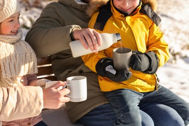 Photo of Happy family warming themselves with hot tea outdoors on sunny winter day, closeup