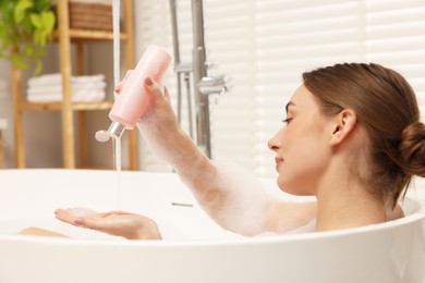 Woman pouring shower gel onto hand in bath indoors