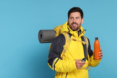 Photo of Happy man with backpack and thermo bottle on light blue background, space for text. Active tourism