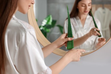 Photo of Young woman applying aloe gel from leaf onto her hand near mirror in bathroom, closeup