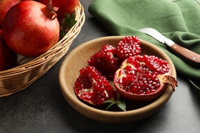 Photo of Fresh pomegranates, green leaves and knife on grey table