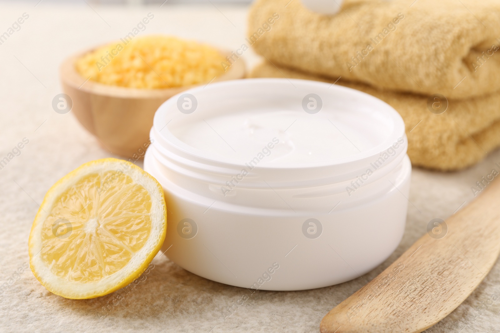 Photo of Body care. Composition with moisturizing cream in open jar and half of lemon on light textured table, closeup