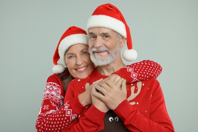 Photo of Happy senior couple in Christmas sweaters and Santa hats on grey background