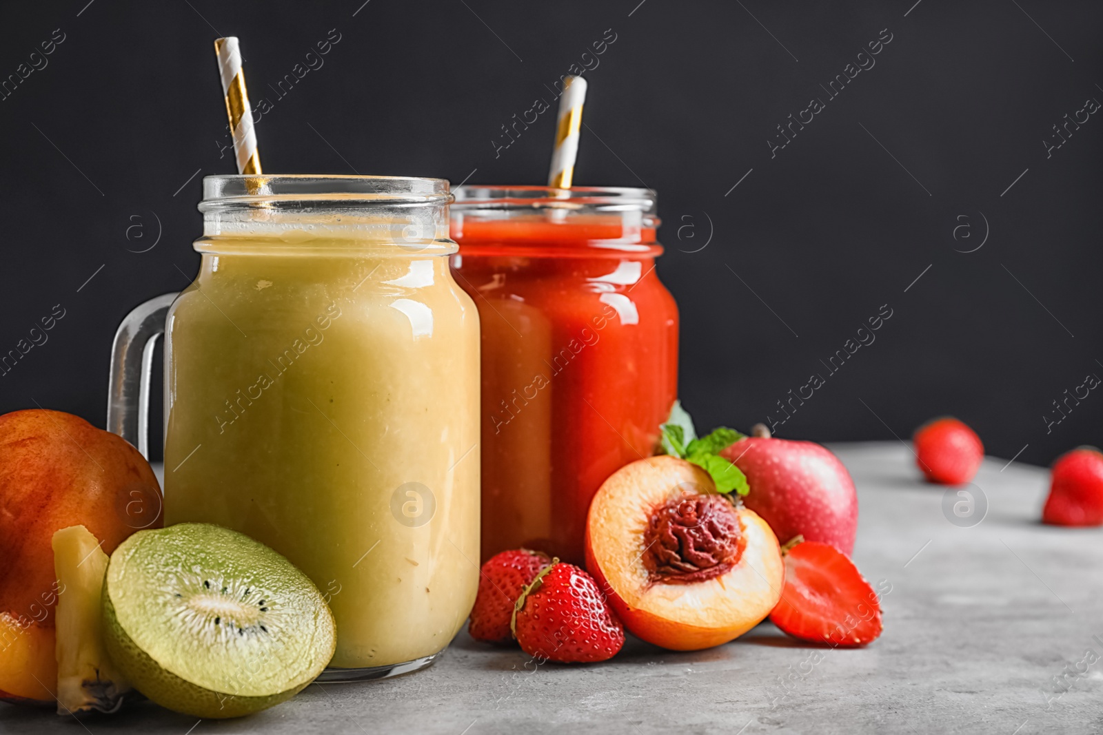 Photo of Delicious juices and fresh ingredients on grey table against black background