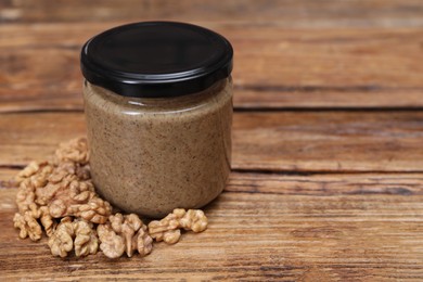 Tasty nut paste in jar and walnuts on wooden table, closeup. Space for text