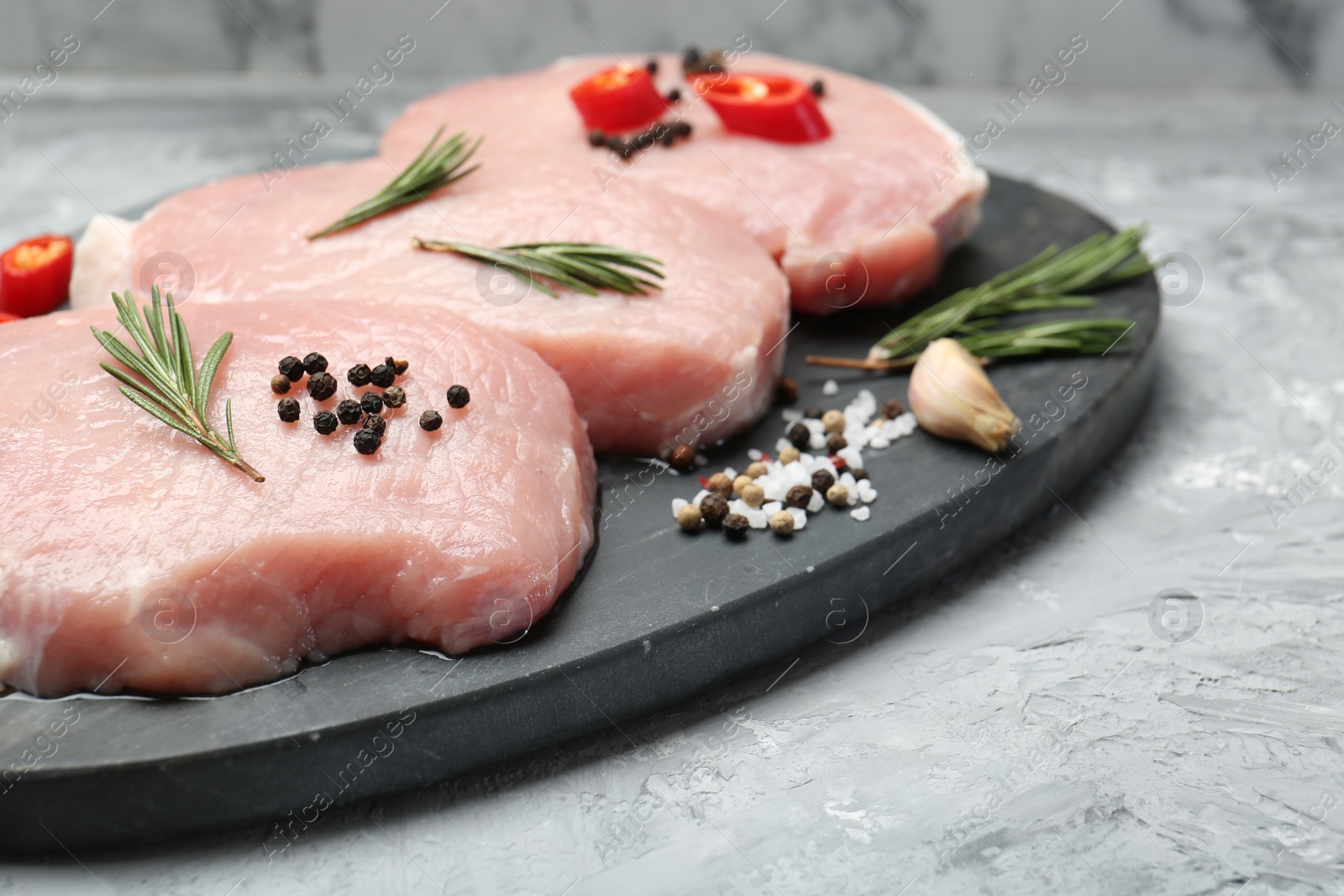 Photo of Pieces of raw pork meat, chili pepper and spices on grey textured table, closeup