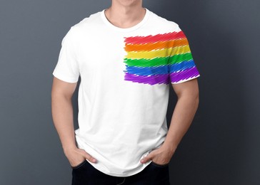 Young man wearing white t-shirt with image of LGBT pride flag on grey background