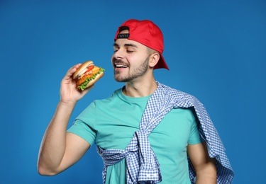 Photo of Handsome man eating tasty burger on color background