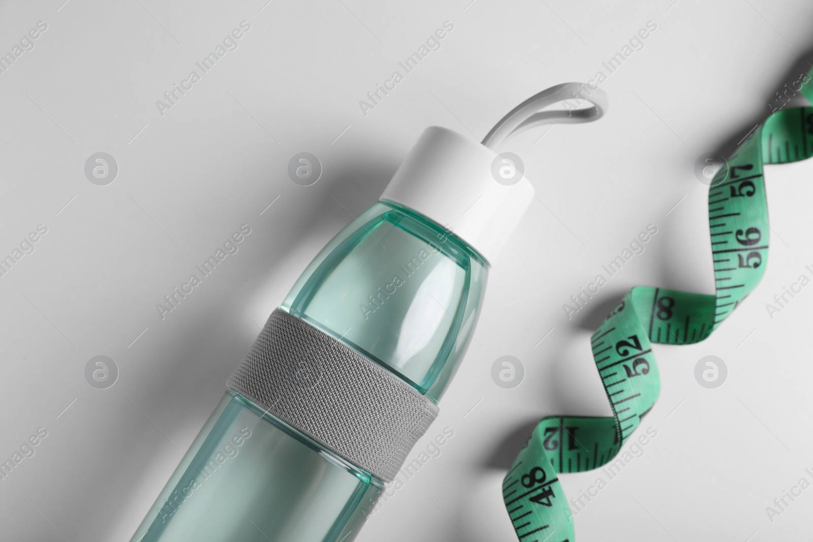 Photo of Measuring tape and bottle with water on white background, flat lay. Weight control concept