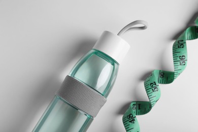 Measuring tape and bottle with water on white background, flat lay. Weight control concept