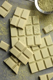 Photo of Pieces of tasty matcha chocolate bars and powder on grey table, flat lay