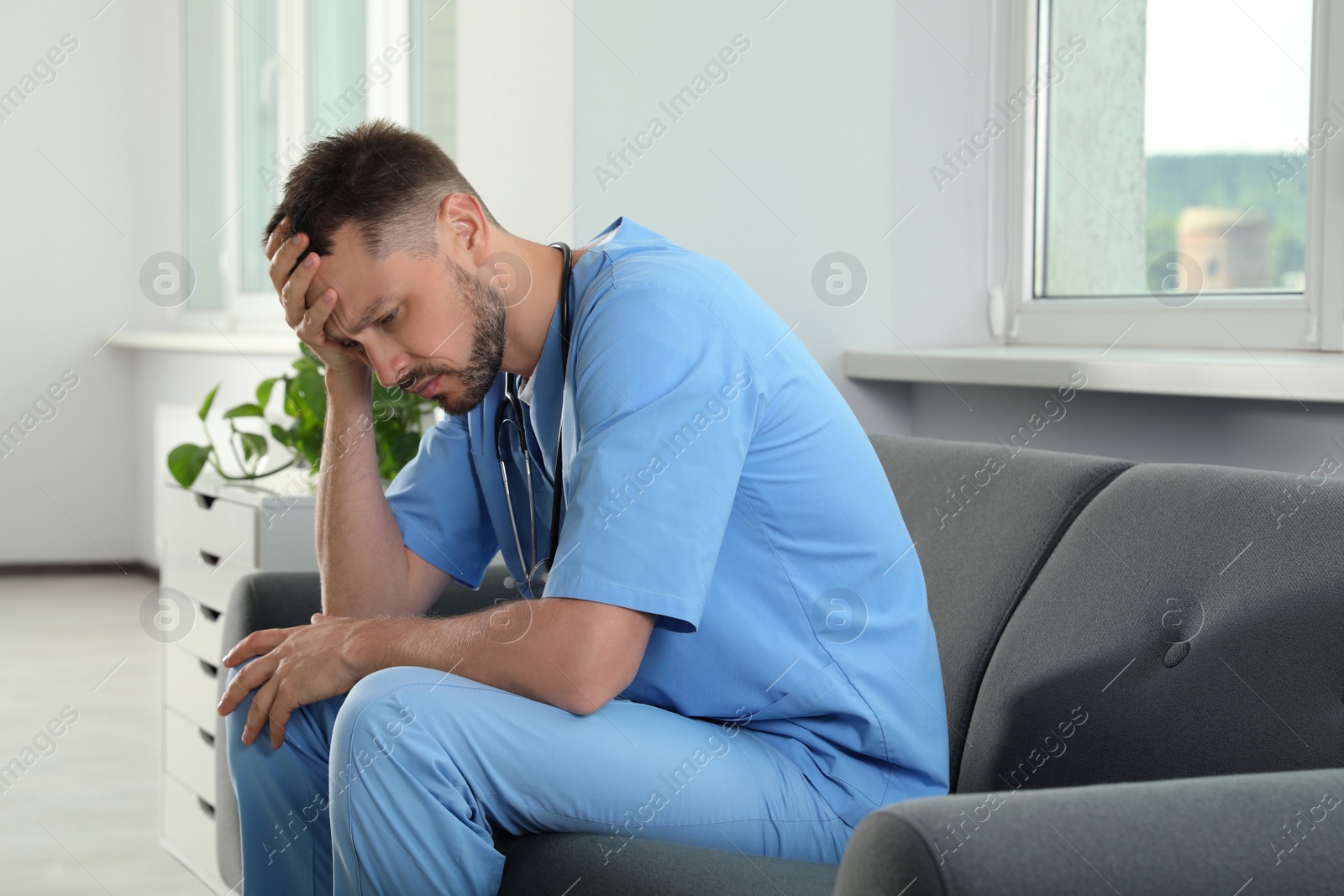 Photo of Exhausted doctor sitting on sofa in hospital