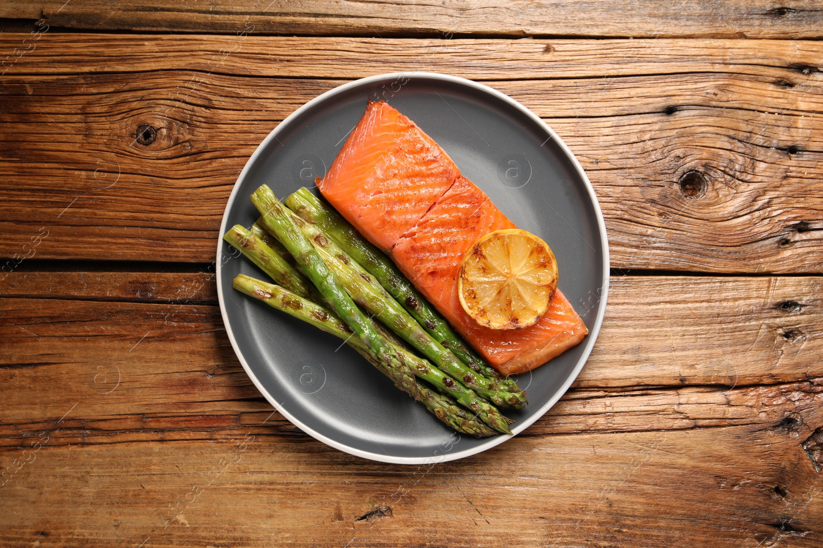 Photo of Tasty grilled salmon with asparagus and lemon on wooden table, top view