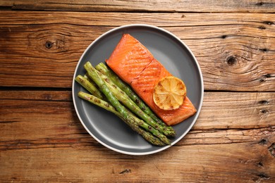 Photo of Tasty grilled salmon with asparagus and lemon on wooden table, top view