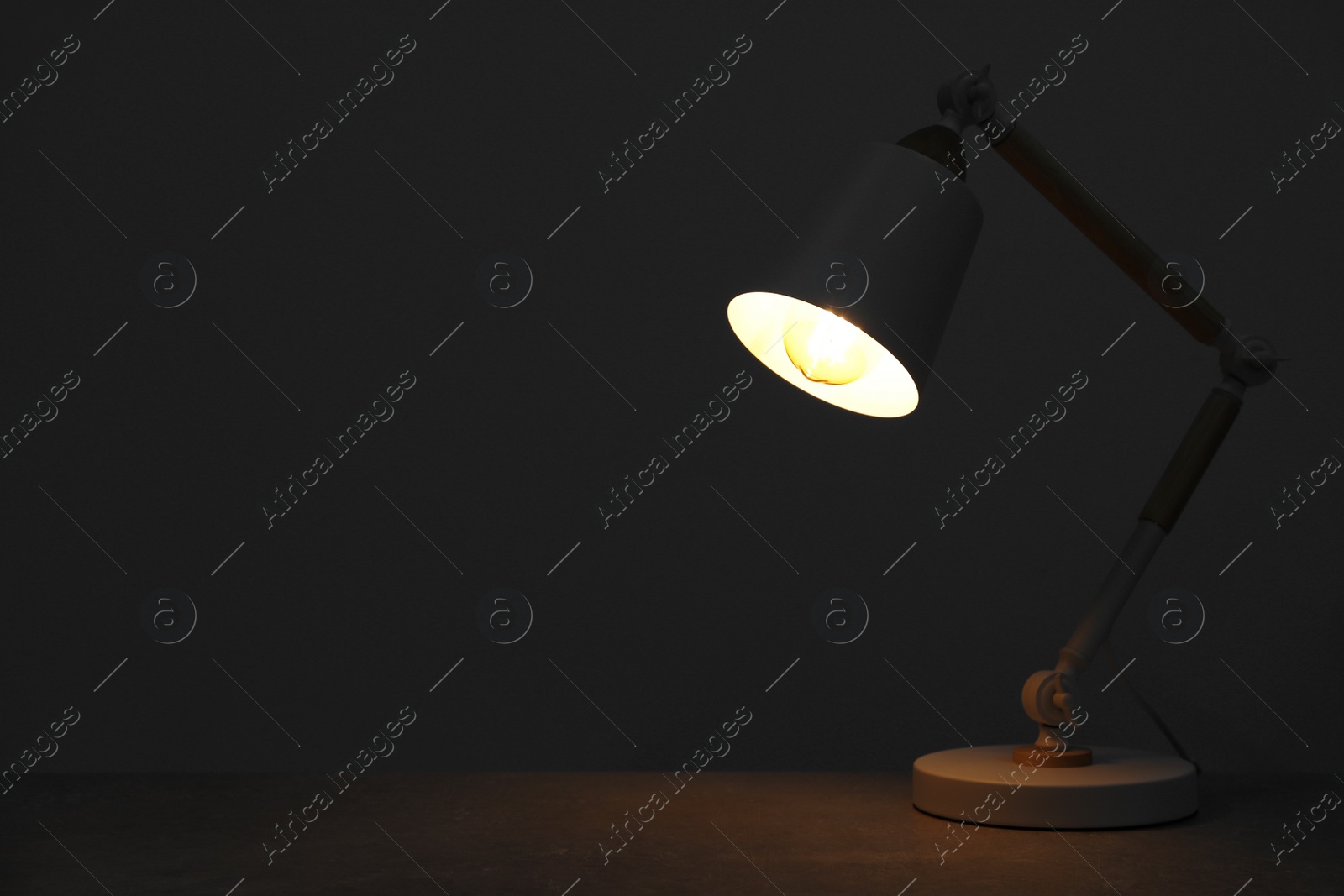 Photo of Stylish modern desk lamp on wooden table at night, space for text