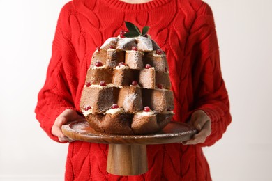 Woman holding delicious Pandoro Christmas tree cake decorated with powdered sugar and berries indoors, closeup