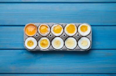 Boiled chicken eggs of different readiness stages in carton on blue wooden table, top view