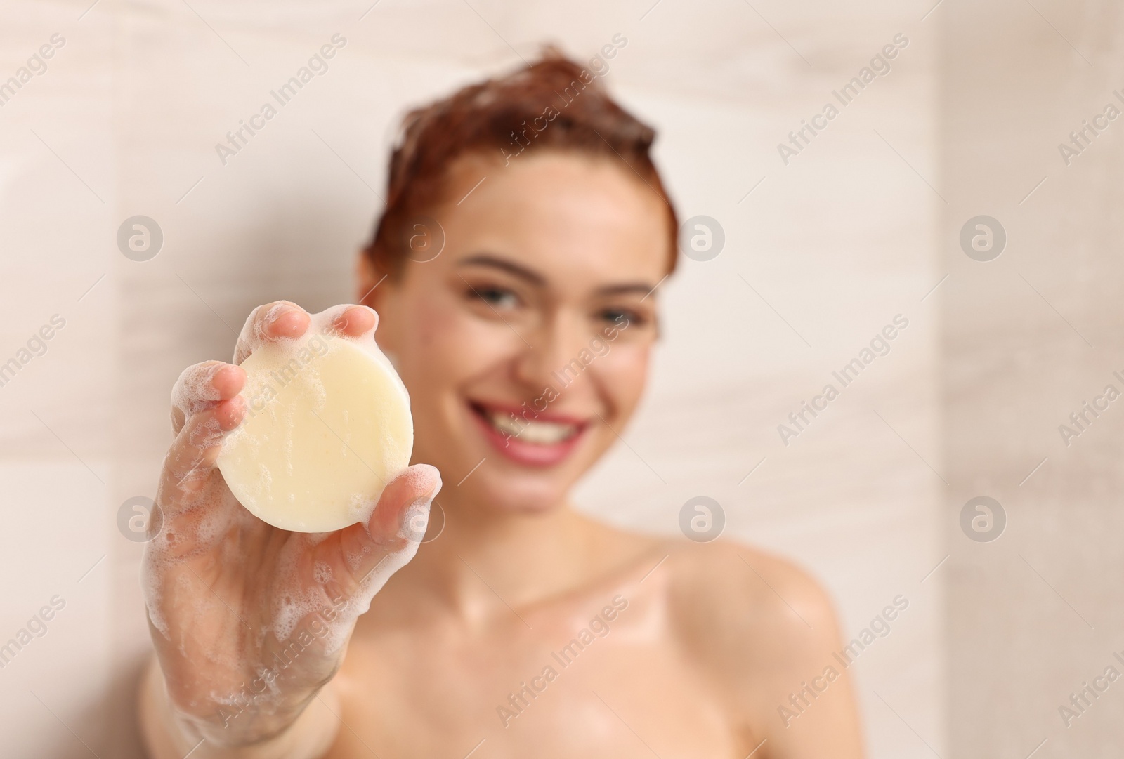 Photo of Happy young woman with solid shampoo bar in shower, selective focus. Space for text