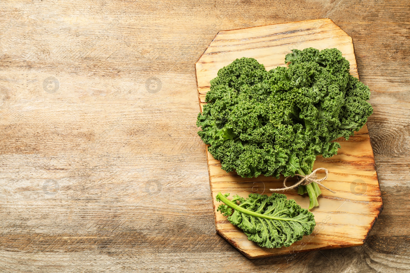 Photo of Fresh kale leaves on wooden table, top view. Space for text