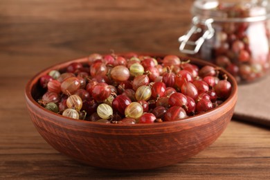 Bowl full of ripe gooseberries on wooden table, closeup