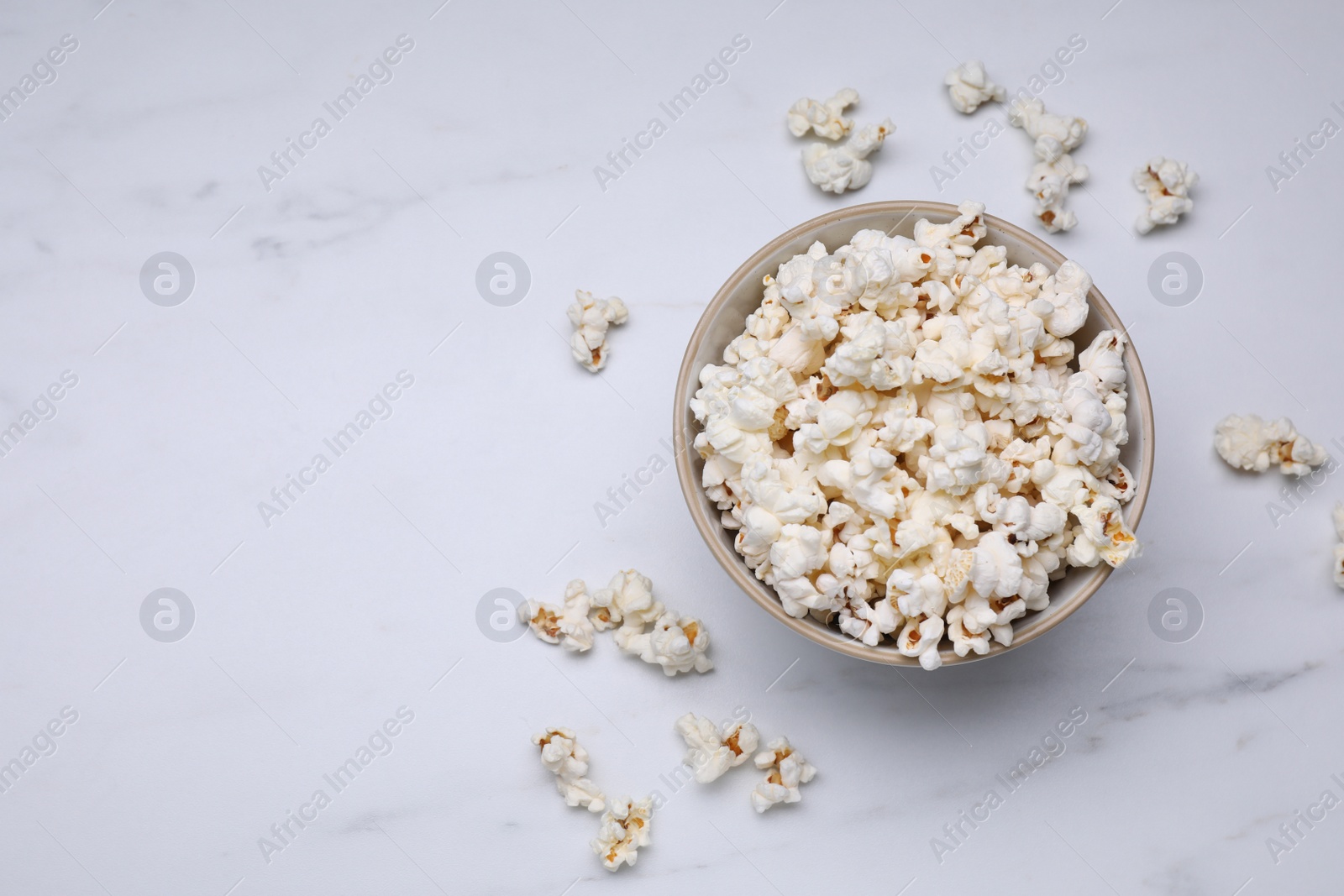 Photo of Bowl of tasty popcorn on white marble table, flat lay. Space for text