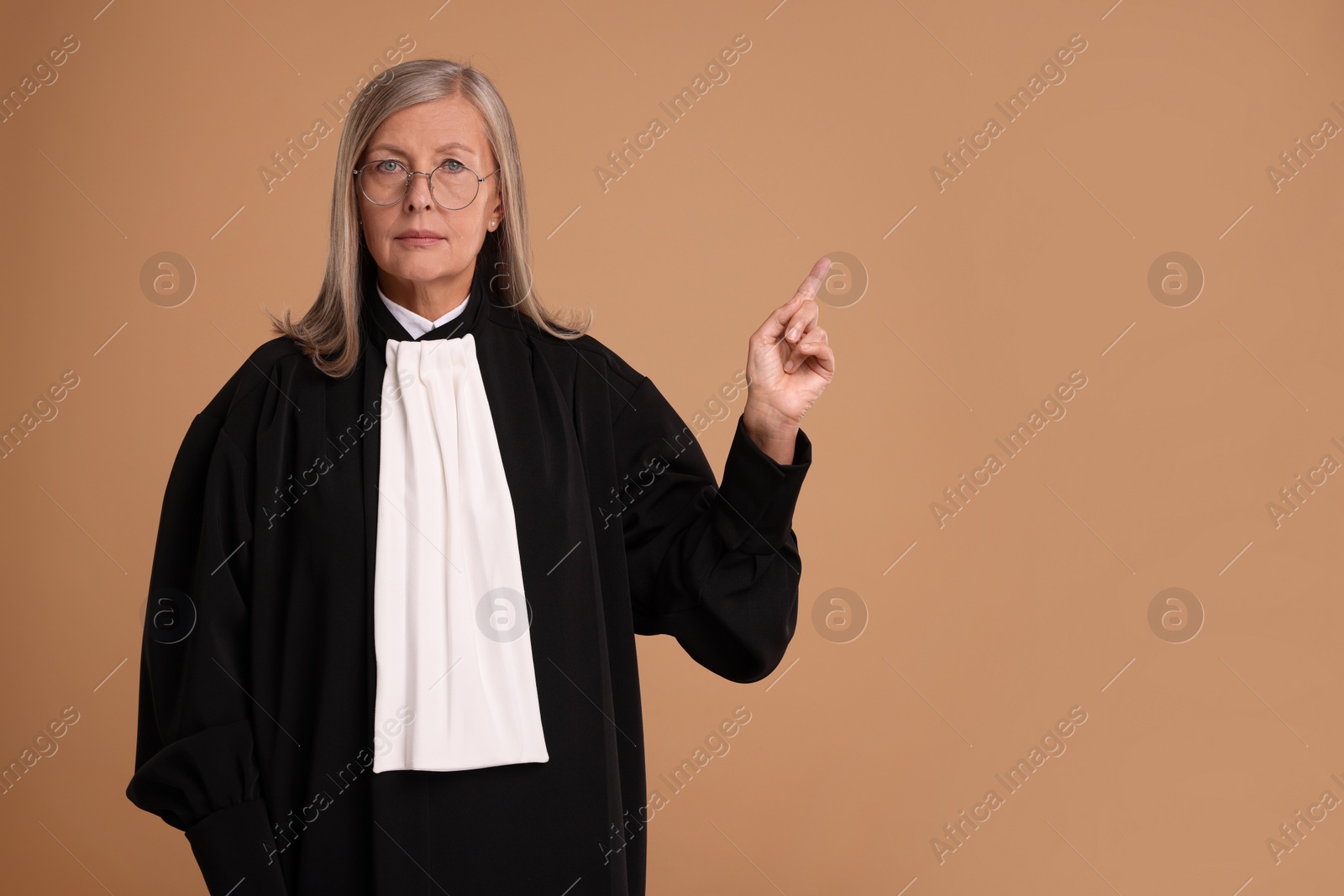 Photo of Senior judge pointing at something on light brown background. Space for text