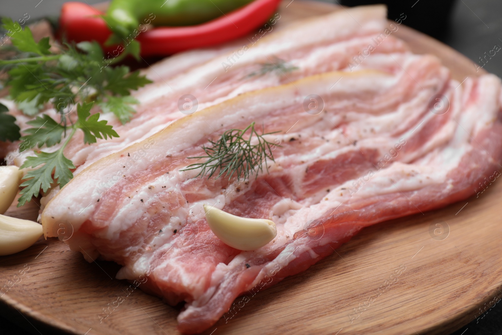 Photo of Tasty pork fatback with spices, garlic and herbs on wooden plate, closeup