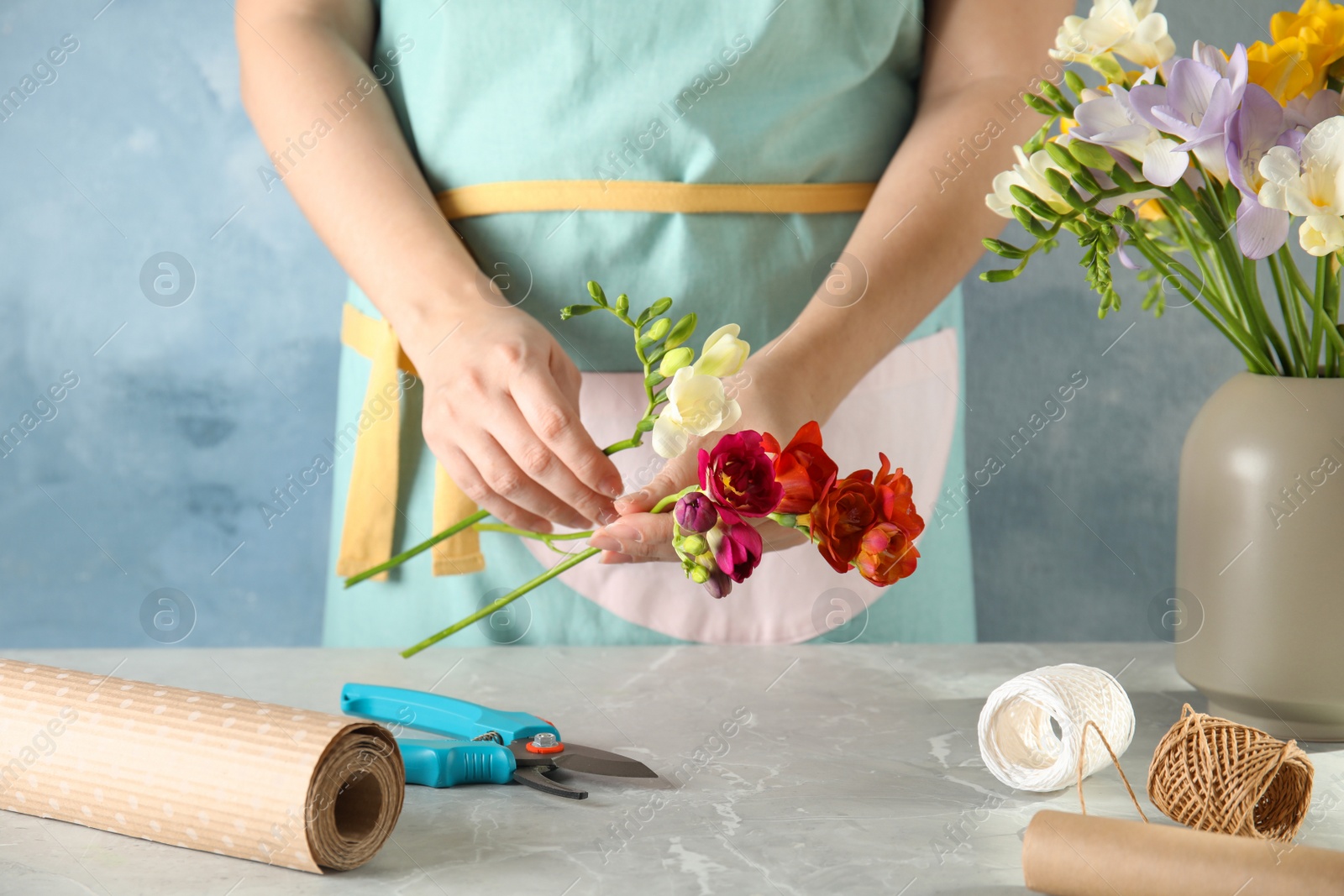 Photo of Woman making bouquet of freesia flowers at table