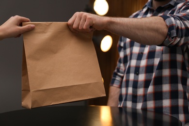 Man giving paper bag with order to customer in cafe, closeup. Mock up for design