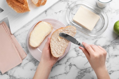 Woman spreading butter on slice of bread over table, closeup