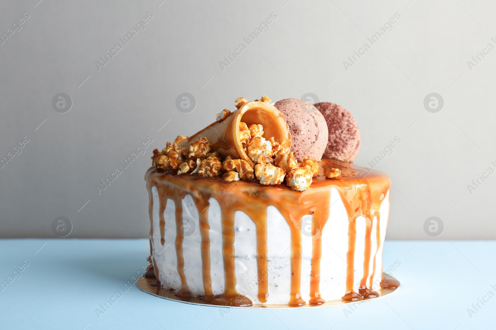 Photo of Delicious homemade cake with caramel sauce and popcorn on table against color background