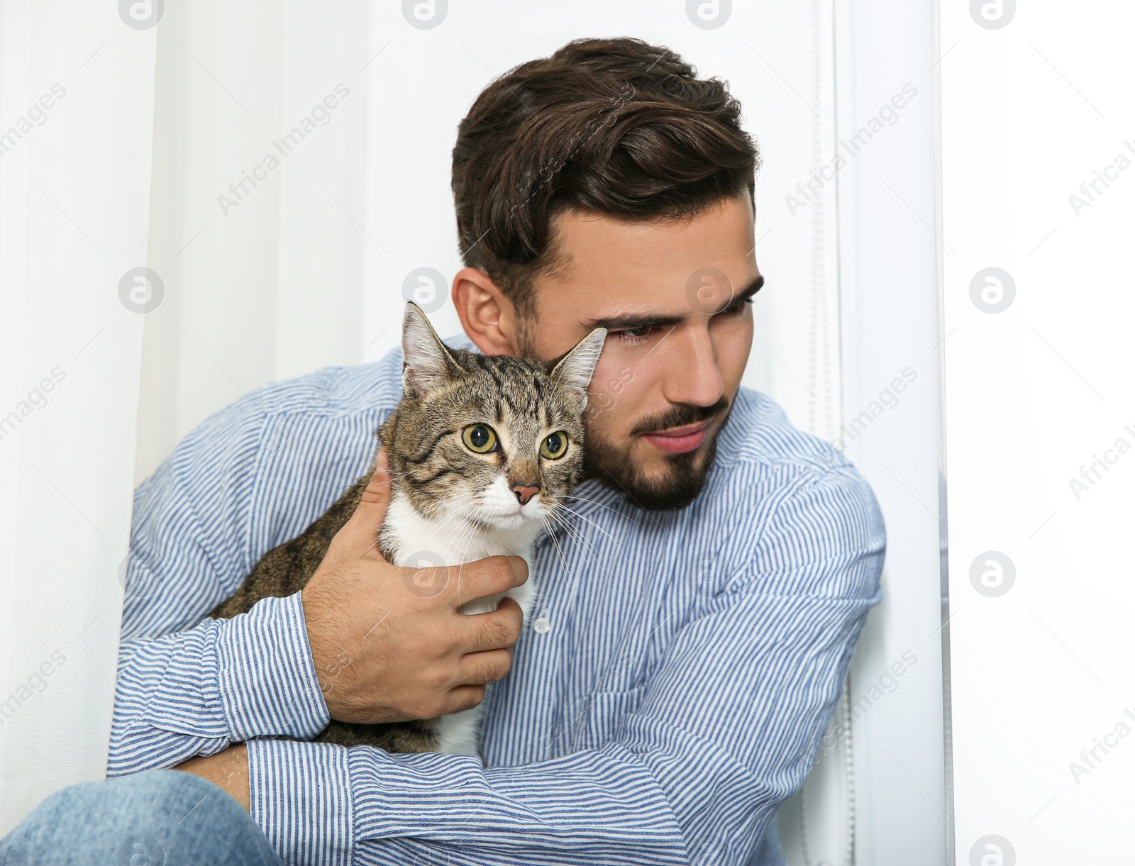 Photo of Man with tabby cat near window at home. Friendly pet