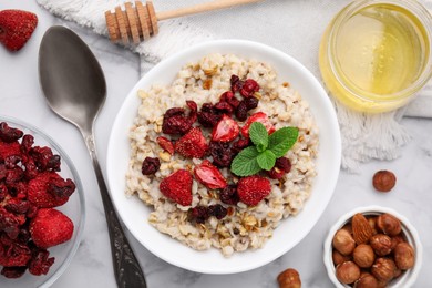 Photo of Oatmeal with freeze dried strawberries and mint served with honey and hazelnuts on white marble table, flat lay