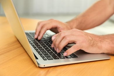 Photo of Man using laptop for search at wooden table indoors, closeup