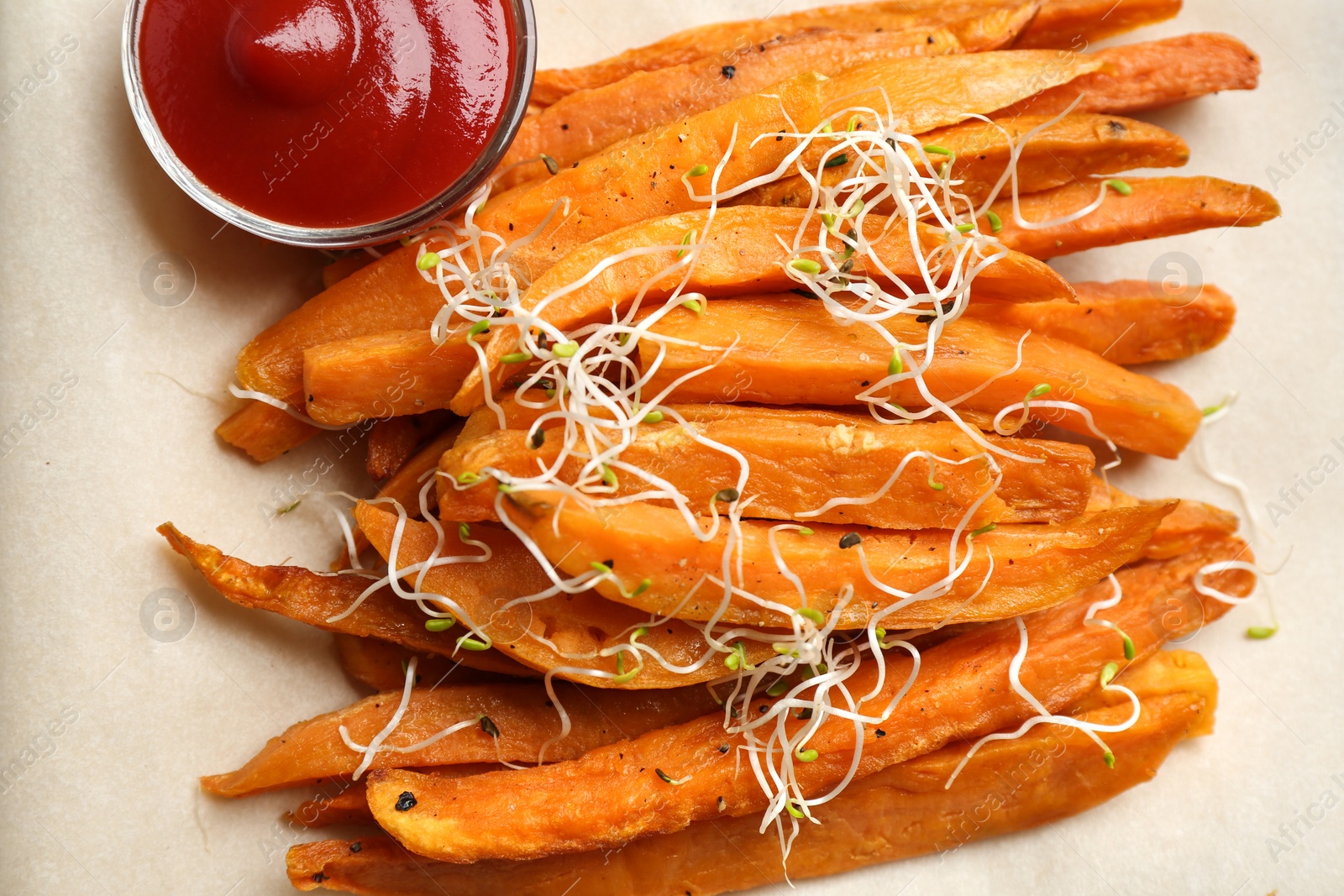 Photo of Tasty sweet potato fries on parchment, top view