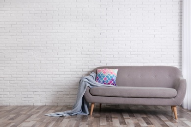 Photo of Minimalist living room interior with cozy sofa, pillow and plaid near brick wall. Space for text