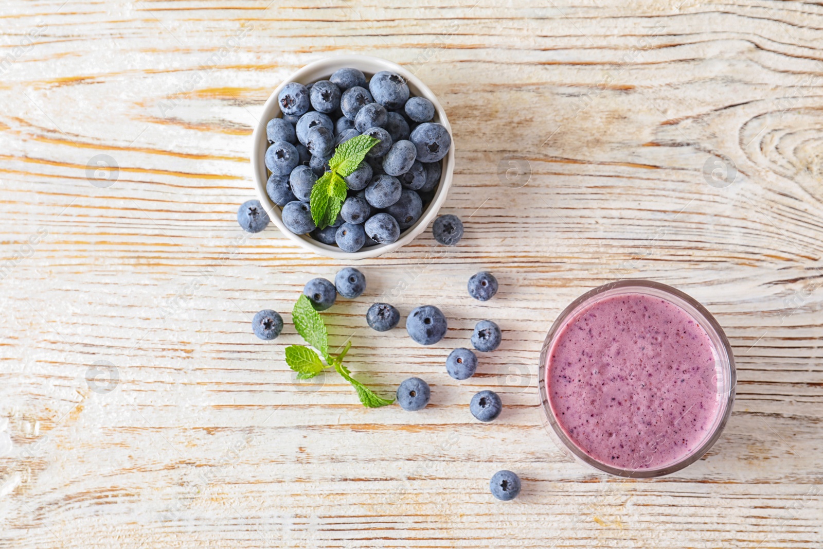 Photo of Tasty blueberry smoothie in glass and bowl with fresh berries on wooden table, top view