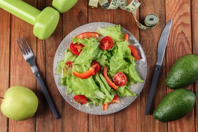 Photo of Healthy diet. Salad, cutlery, dumbbells and measuring tape on wooden table, flat lay