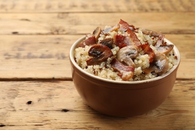 Photo of Tasty quinoa porridge with fried bacon and mushrooms in bowl on wooden table, closeup. Space for text