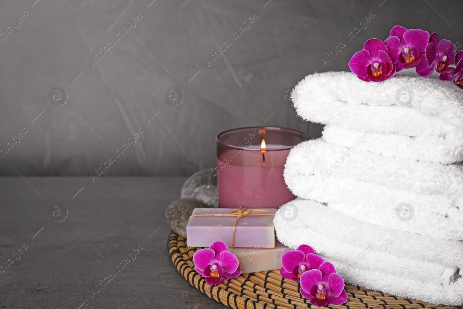 Photo of Composition with towels and orchid flowers on grey stone surface, space for text