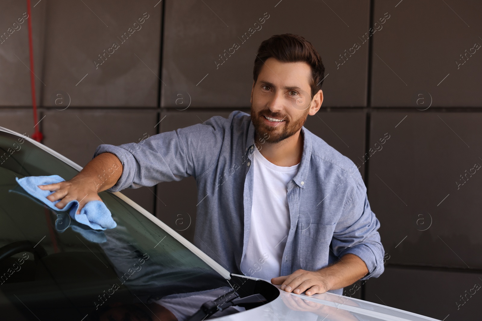 Photo of Smiling man cleaning car windshield with rag outdoors