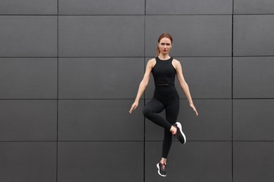 Photo of Beautiful woman in gym clothes jumping near dark grey wall on street, space for text
