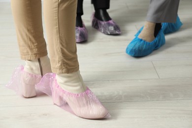 Photo of Women wearing pink shoe covers onto different footwear indoors, selective focus