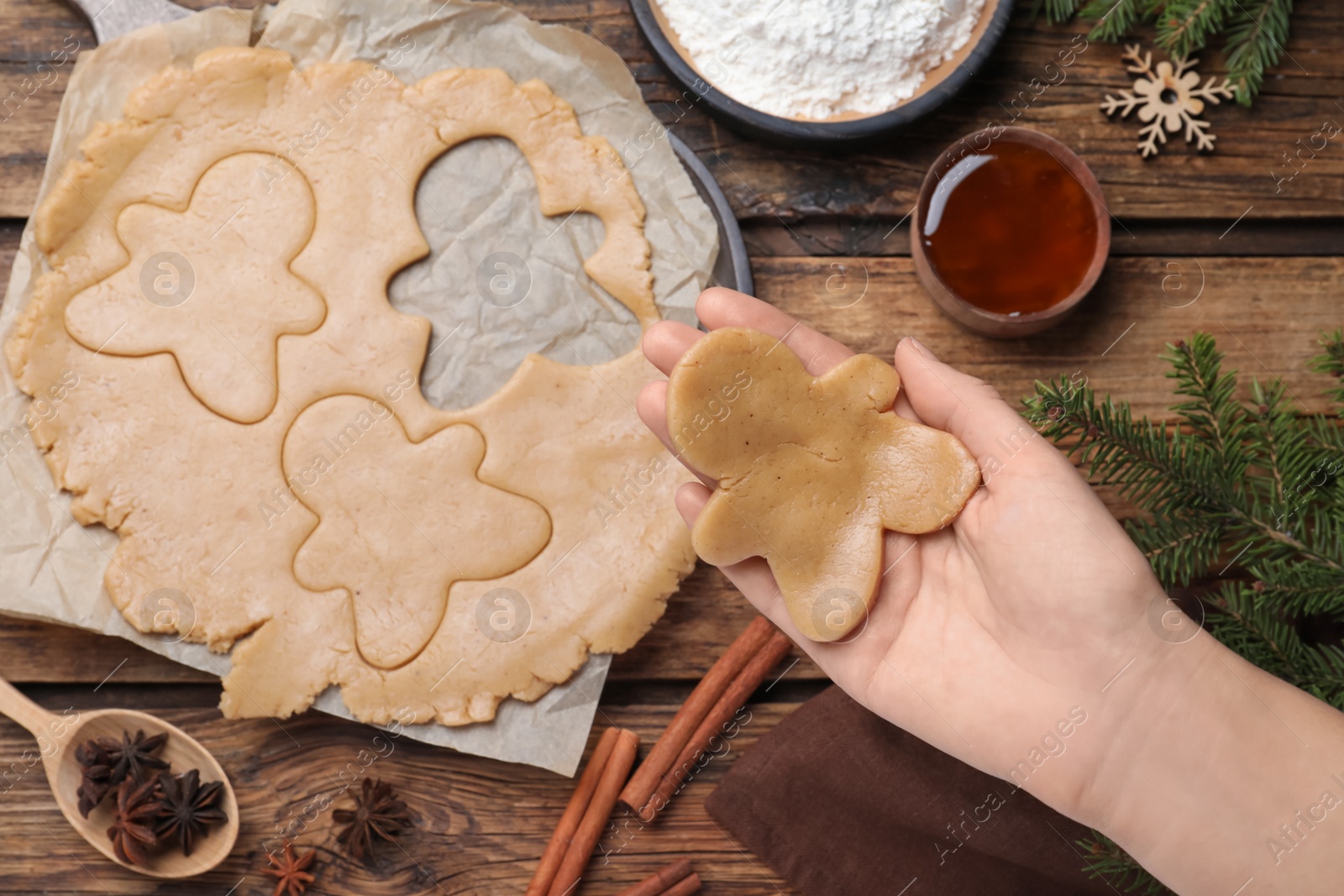 Photo of Making homemade Christmas cookies. Woman holding gingerbread man above wooden table, top view
