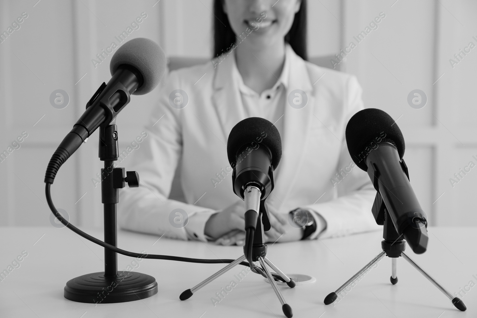 Image of Journalist conference. Businesswoman giving interview at table with microphones indoors, closeup. Black and white effect